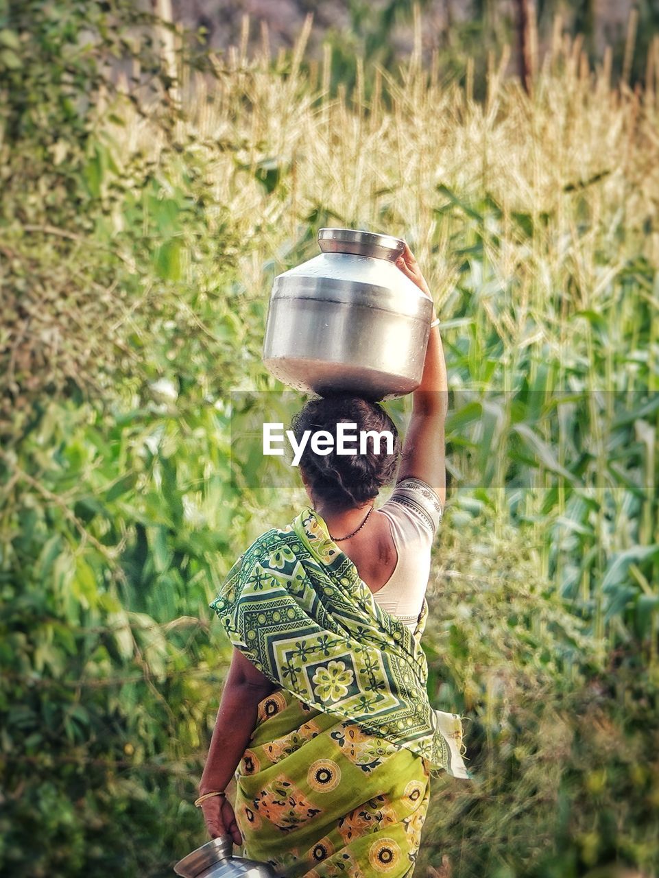 Rear view of woman carrying container on head against plants