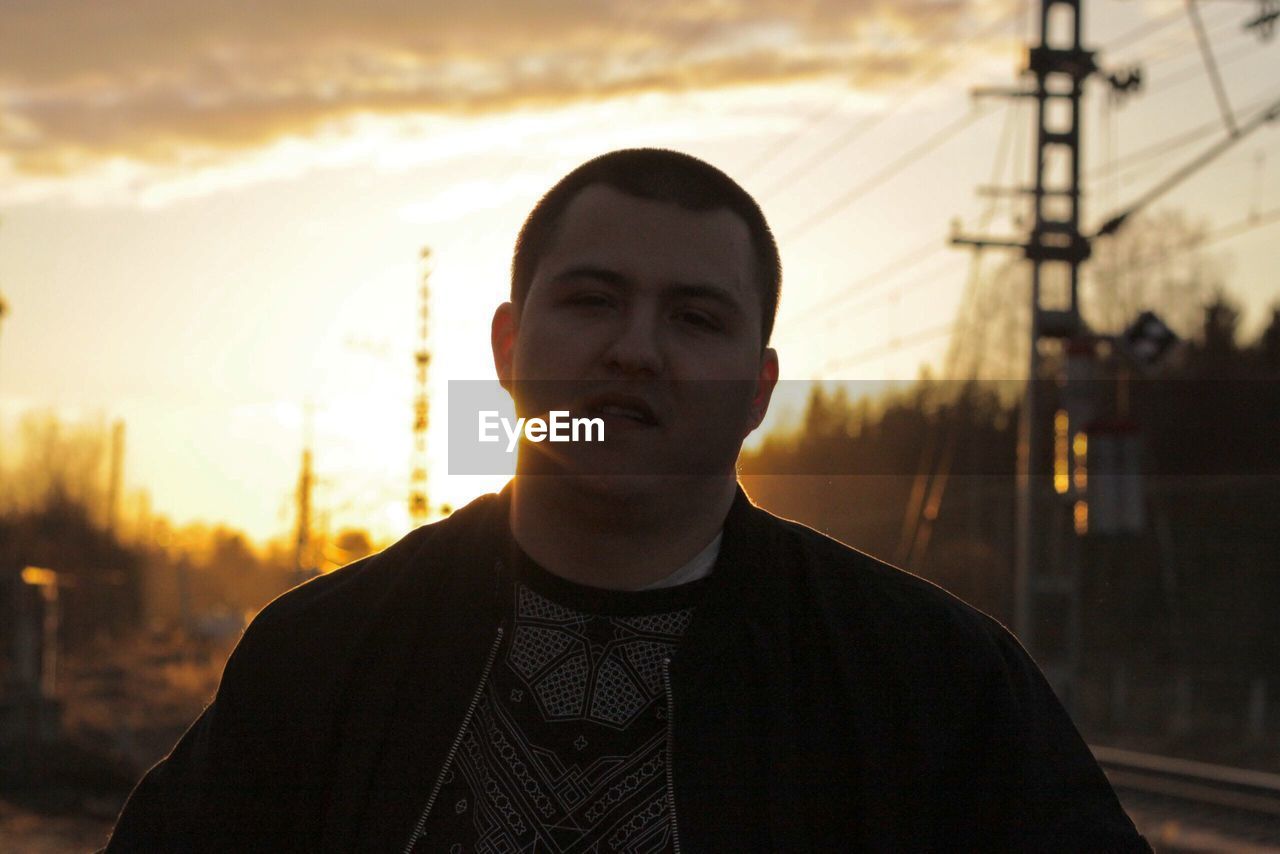 Portrait of young man standing against sky during sunset