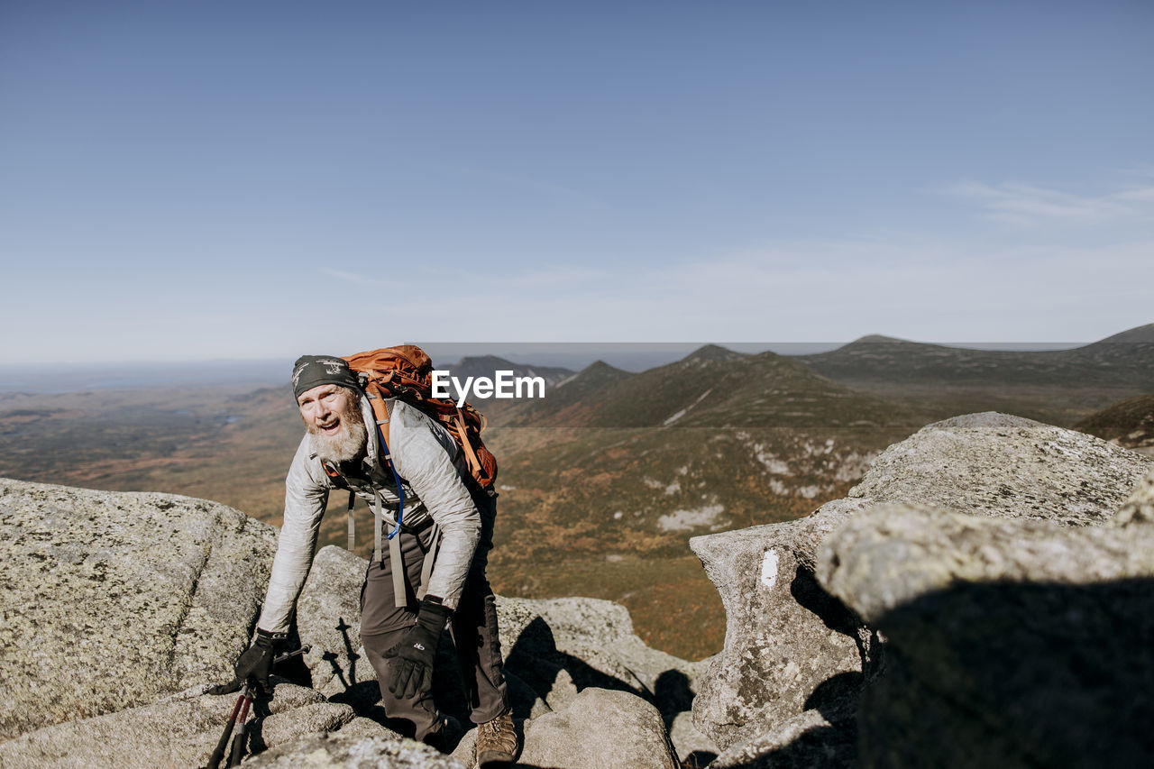 A retired hiker struggles over rocks as he climbs mount katahdin