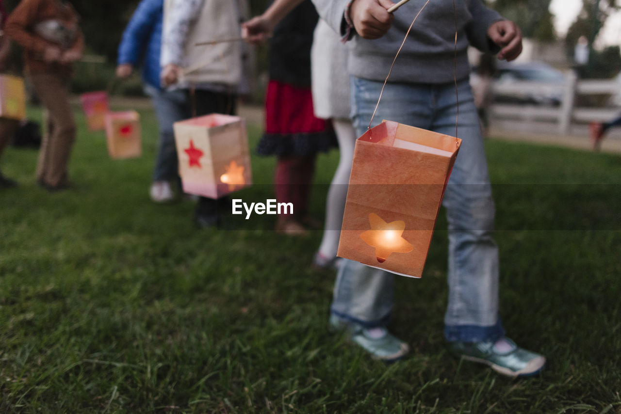 Low section of children carrying illuminated paper lanterns while walking on field