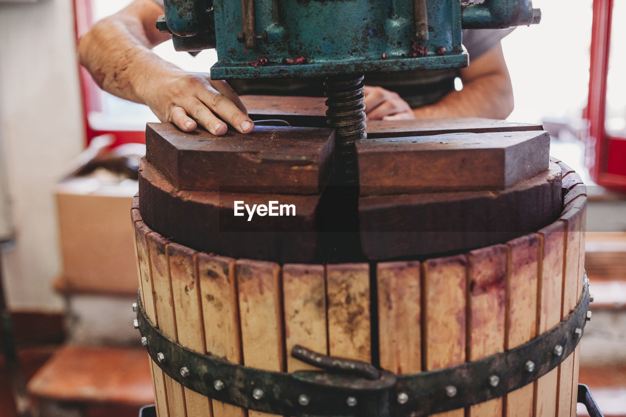 Cropped hands of male vintner using industrial equipment while making wine in cask at factory