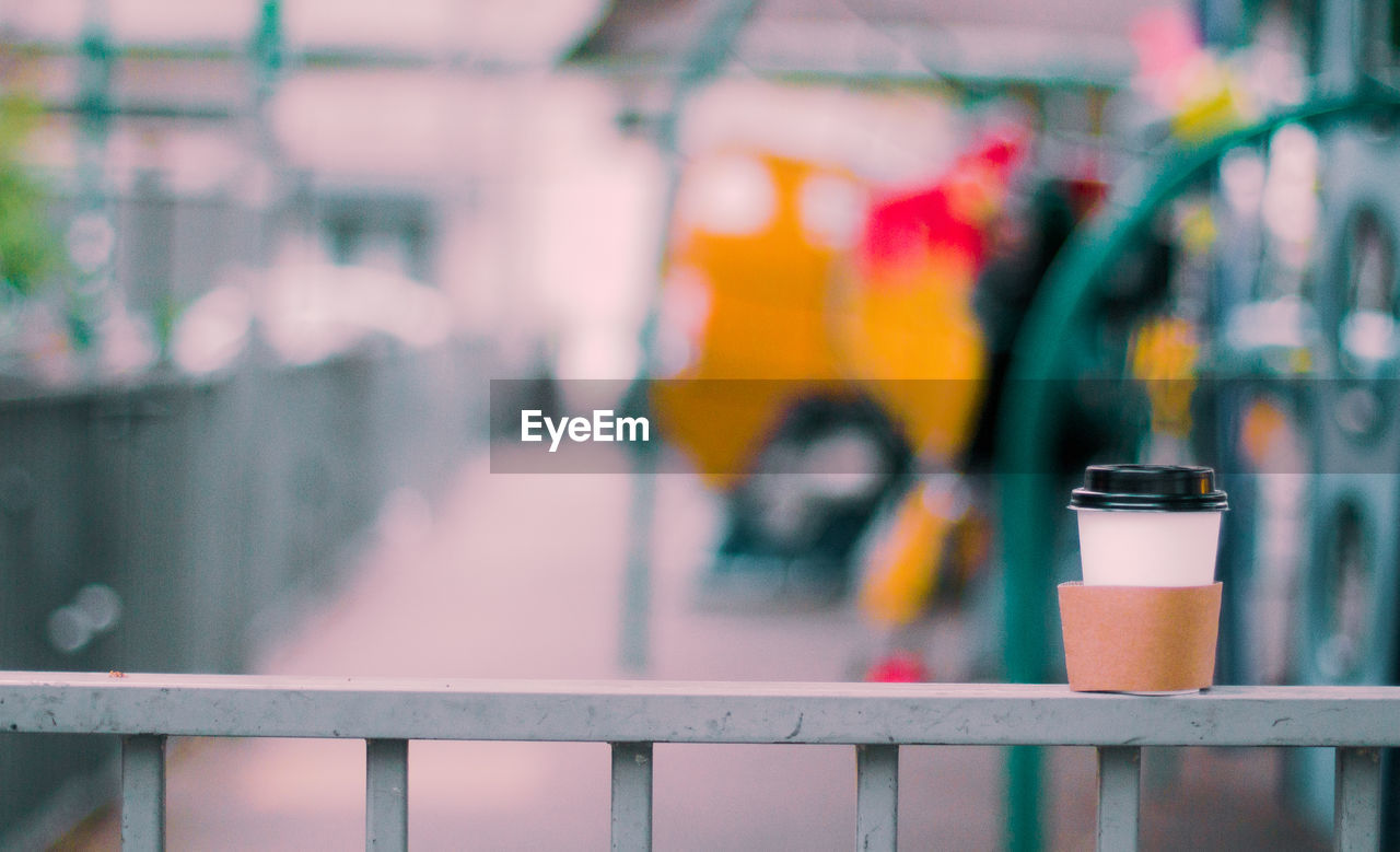 Close-up of metal fence against blurred background  paper coffe cup resting.  