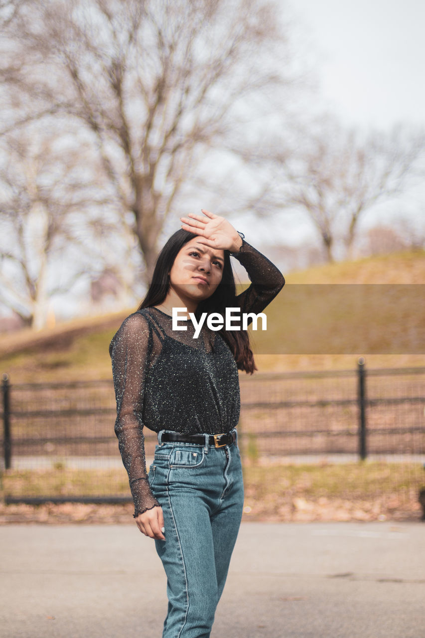 Young woman shielding eyes while standing on road in city