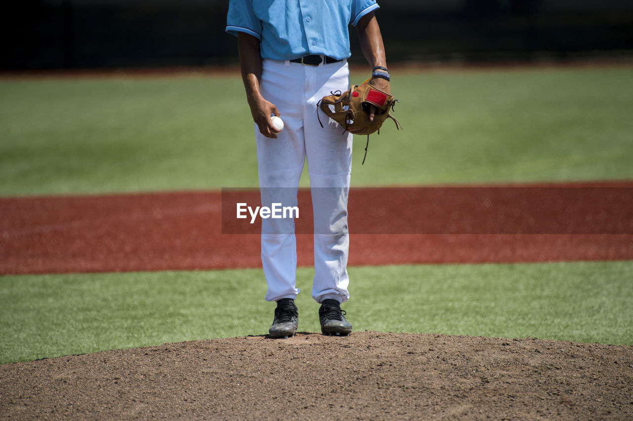 Low section of baseball player standing on playing field during sunny day