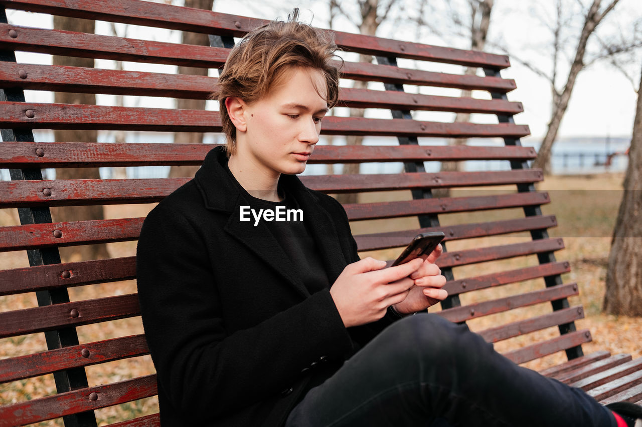 Young man using mobile phone while sitting on bench at park