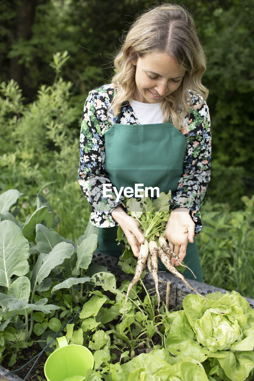 PORTRAIT OF A SMILING WOMAN HOLDING PLANTS