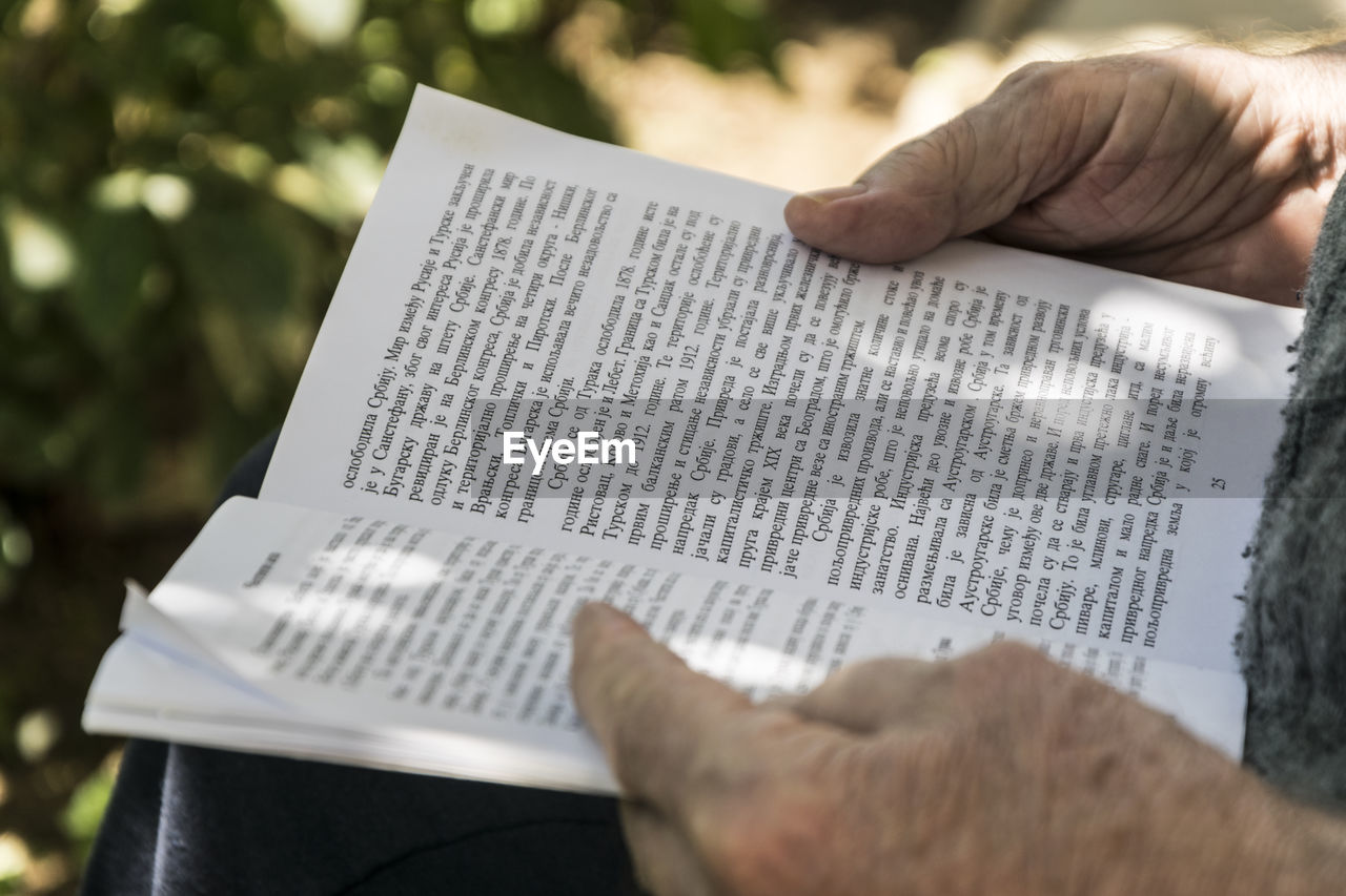 Cropped hands of person reading book outdoors