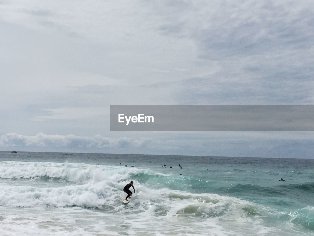 Man surfboarding on sea against cloudy sky