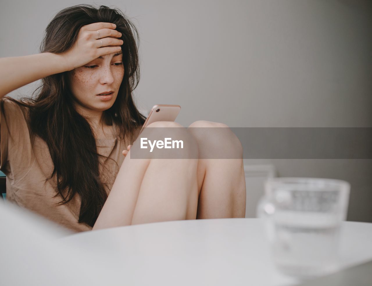 Sad woman with the mobile phone at home in the kitchen by morning