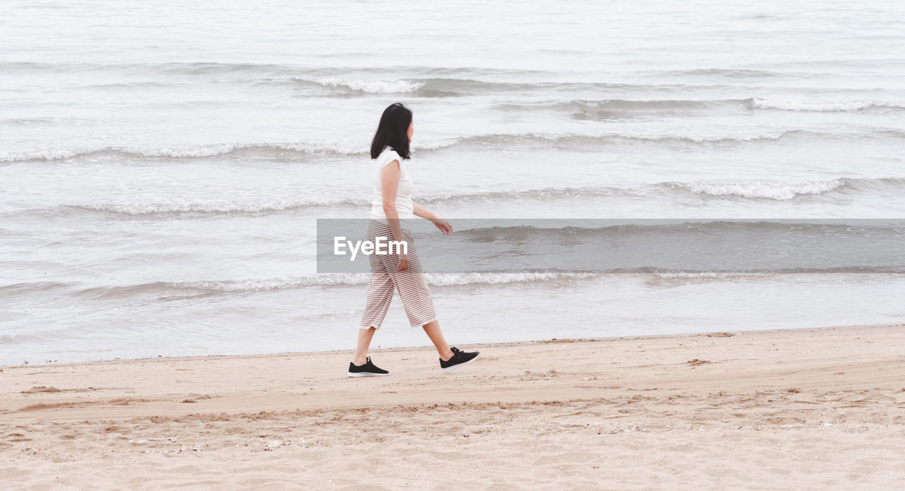 REAR VIEW OF WOMAN STANDING ON SHORE AT BEACH