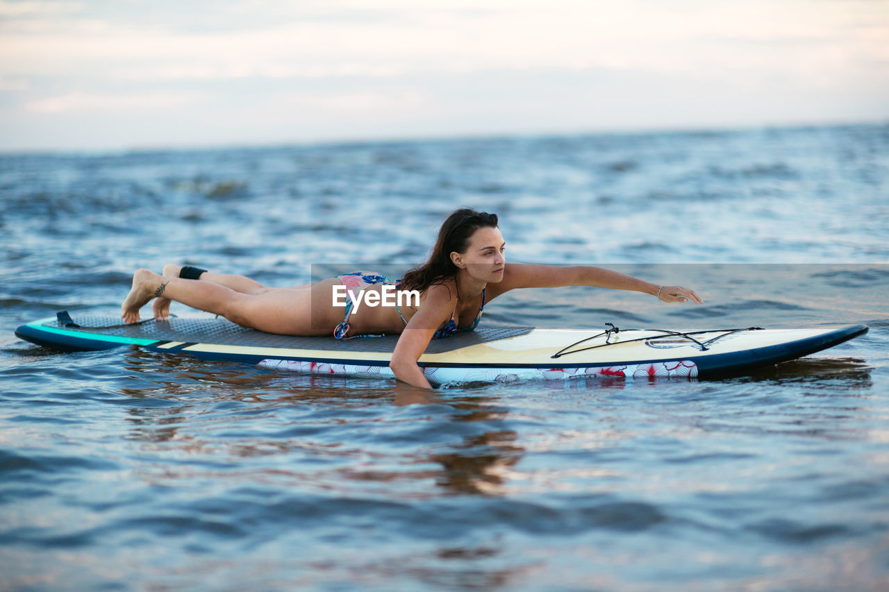 Woman on surfboard in sea against sky