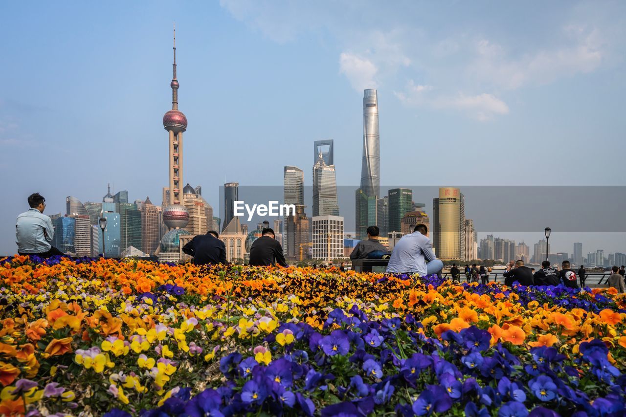 Flowering plants and people against buildings and cloudy sky