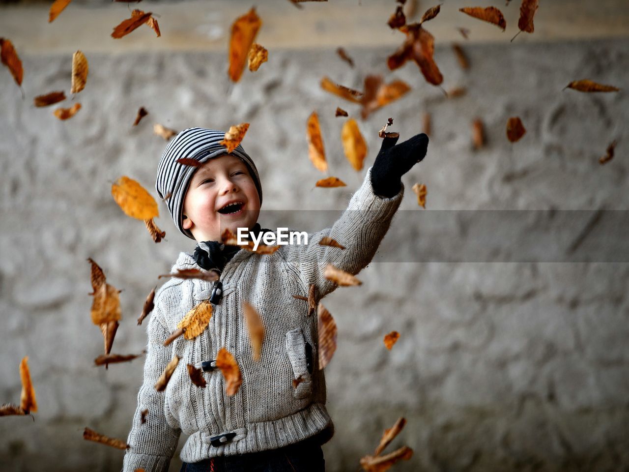 Happy boy in warm clothing playing with leaves