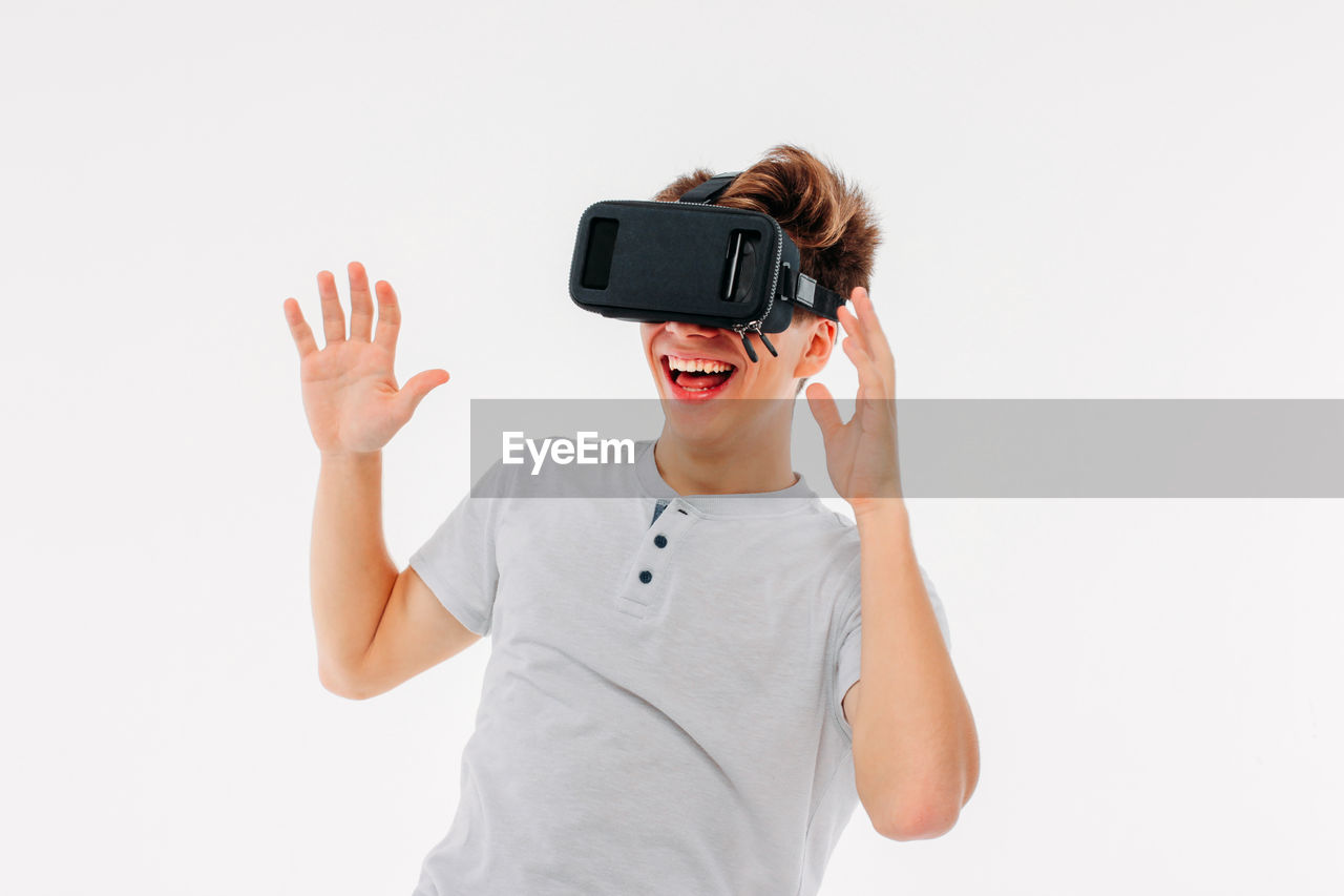 Smiling man wearing virtual reality simulator while gesturing against white background