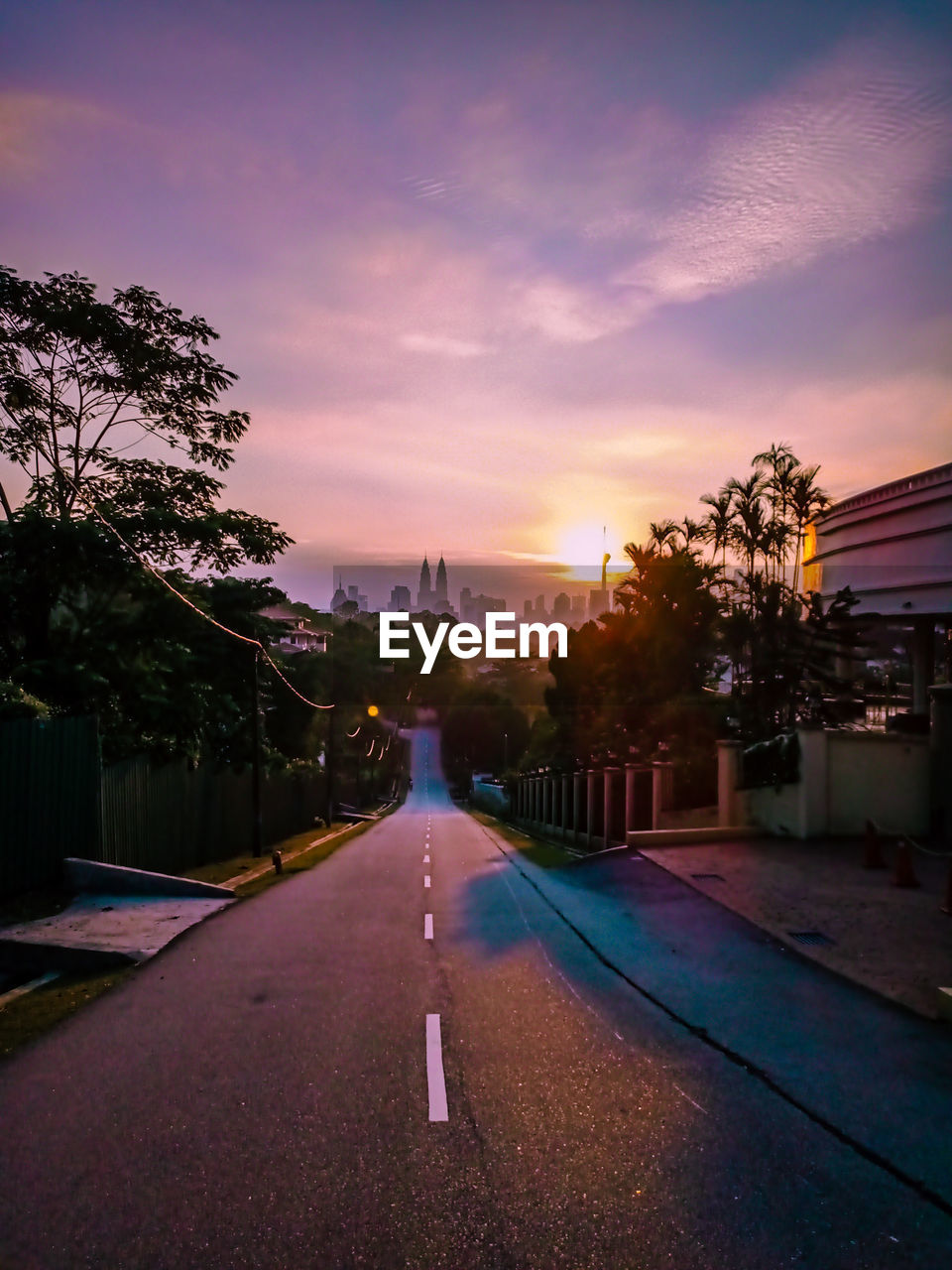 ROAD AMIDST BUILDINGS AGAINST SKY DURING SUNSET