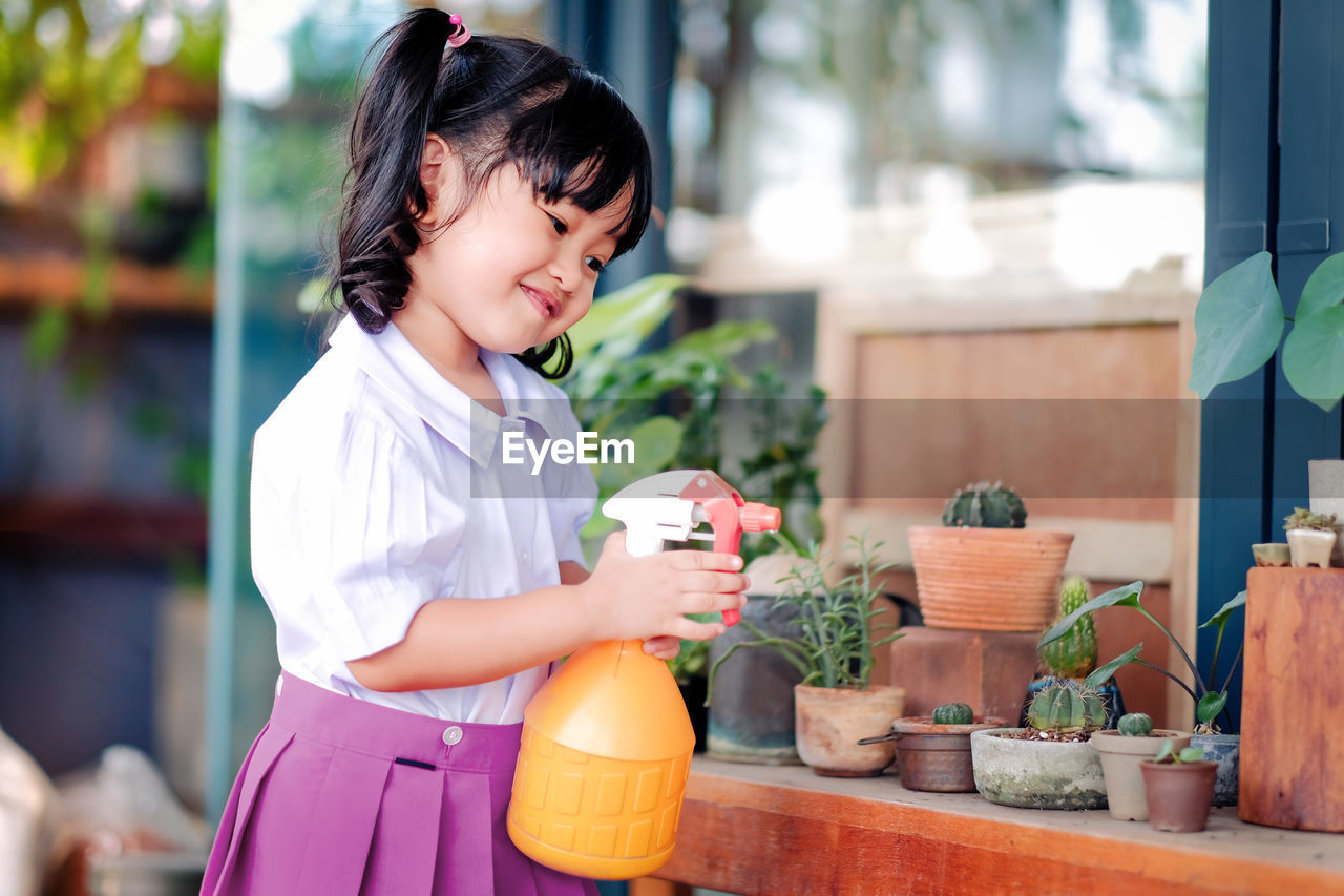 Smiling cute girl spraying water on potted plant