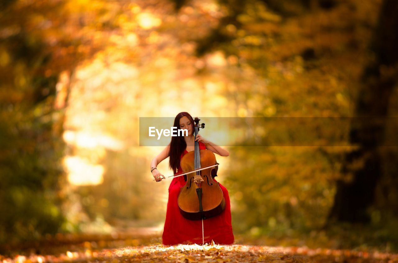 Beautiful woman playing double bass in forest during autumn