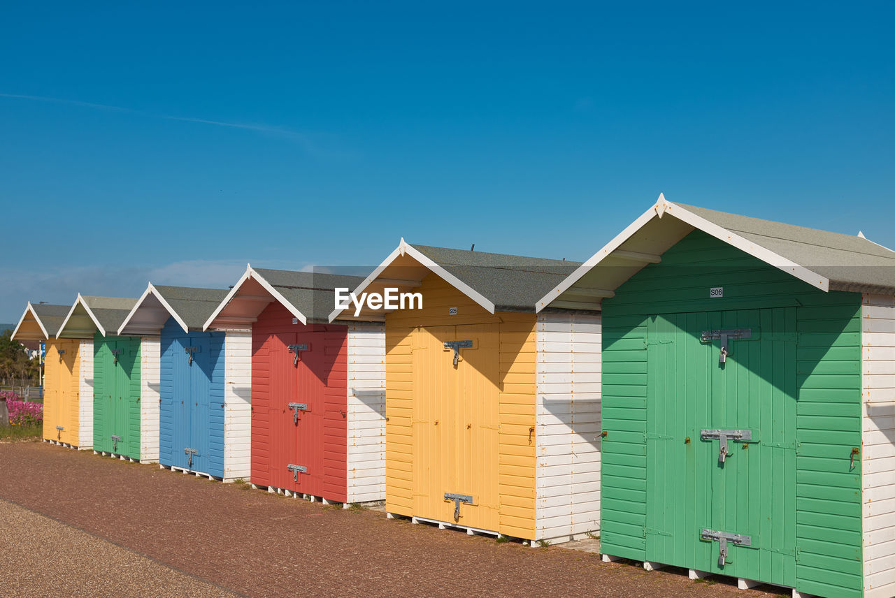 Brightly coloured beach huts with diminishing perspective against a clear blue sky.