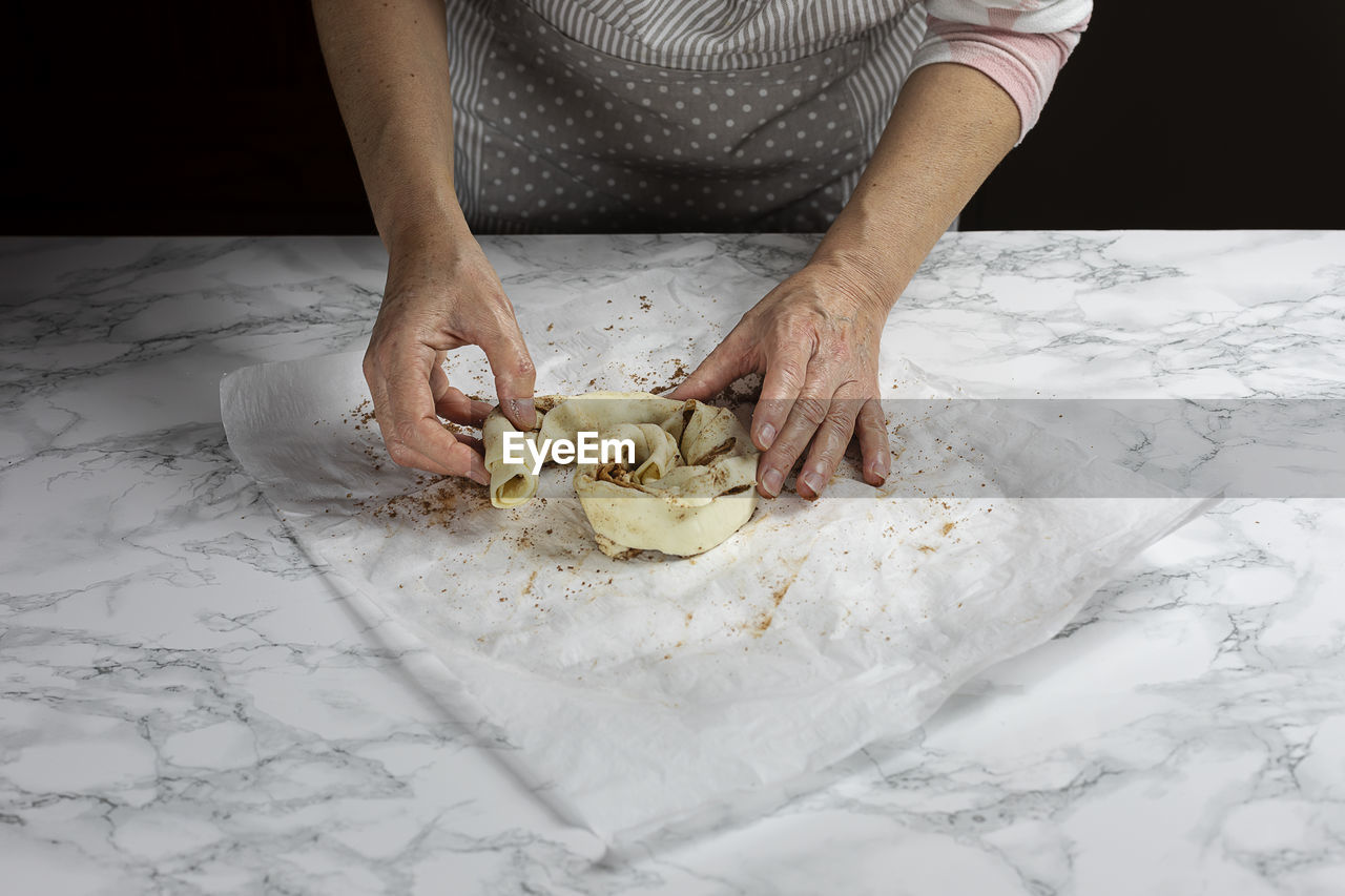 Two female hands roll a puff pastry doughnut before baking it.
