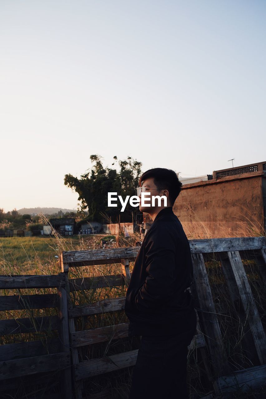 Side view of young man looking away against clear sky