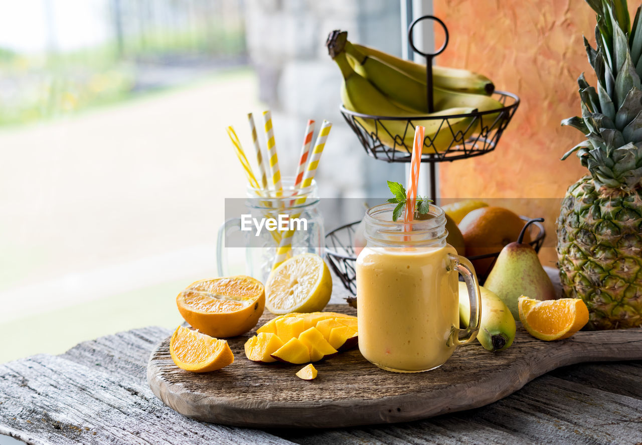 A homemade mango citrus smoothie on a rustic board against a window.