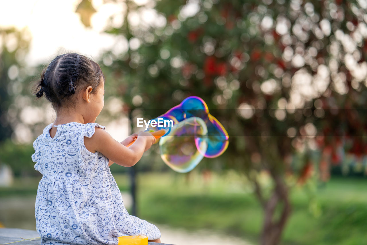 Cute little girl playing with soap bubbles at park.