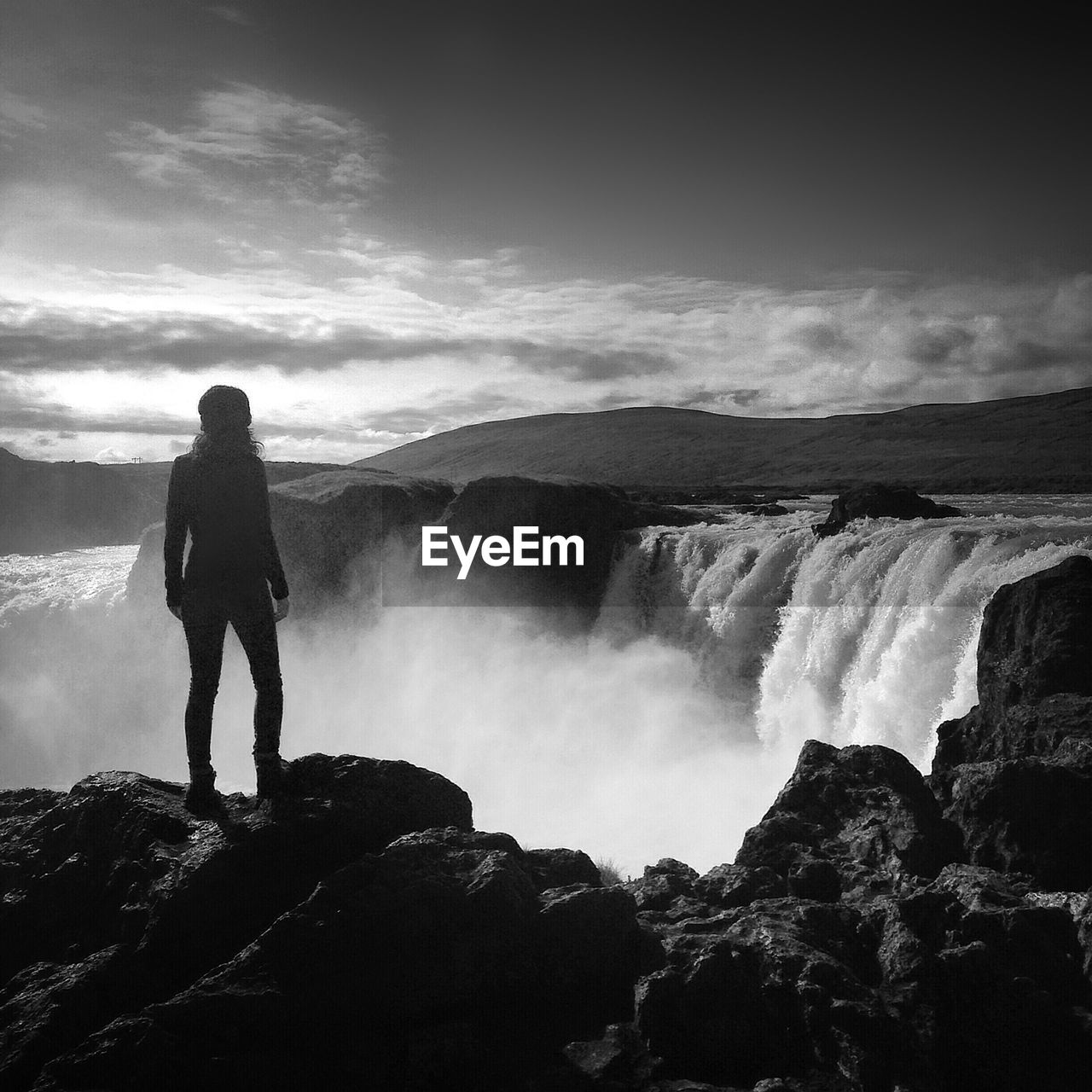 Full length rear view of woman standing on cliff in front waterfall