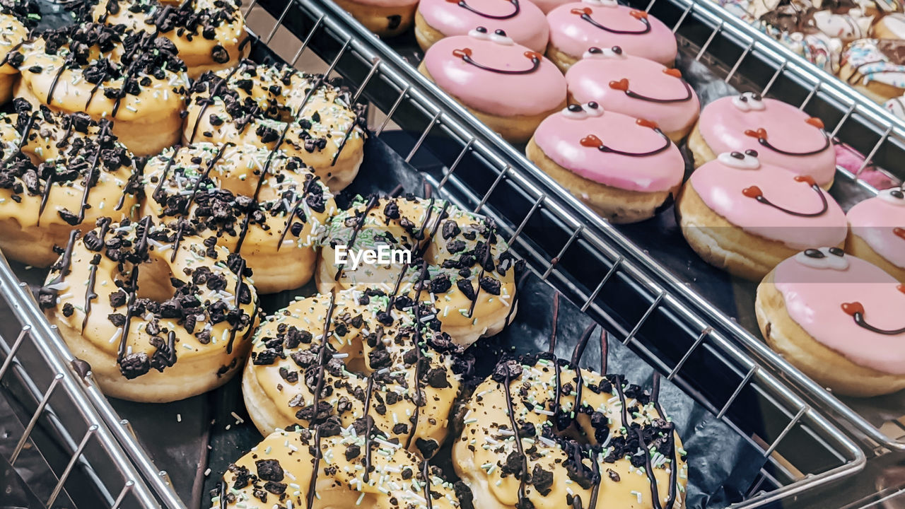Chocolate and pink donuts with smiles in metal trays on a store shelf, close-up side view.