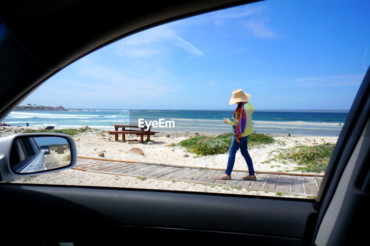 Woman walking on boardwalk at beach seen from car window