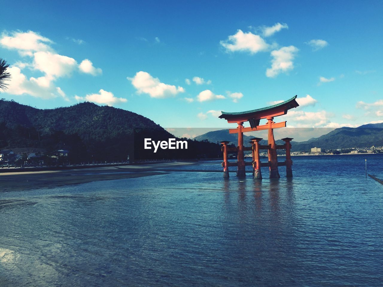 Itsukushima shrine in river against mountains and blue sky