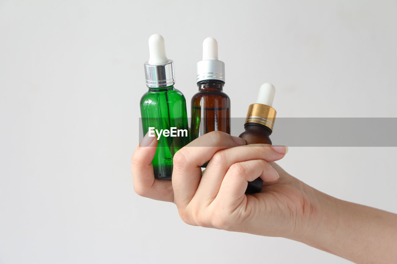 Woman hands holding facial essential oil or serum packaging on white background. 