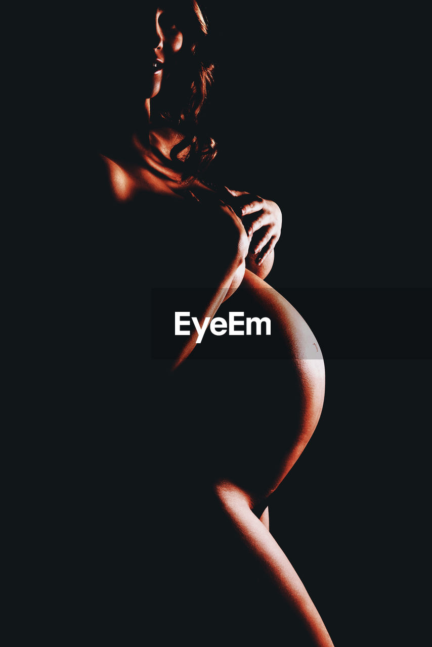 Naked pregnant woman standing against black background