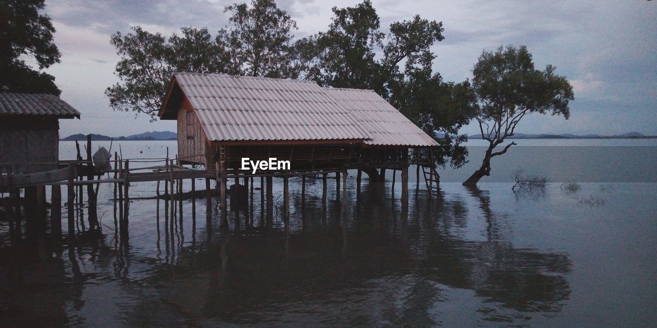 House by lake and trees against sky