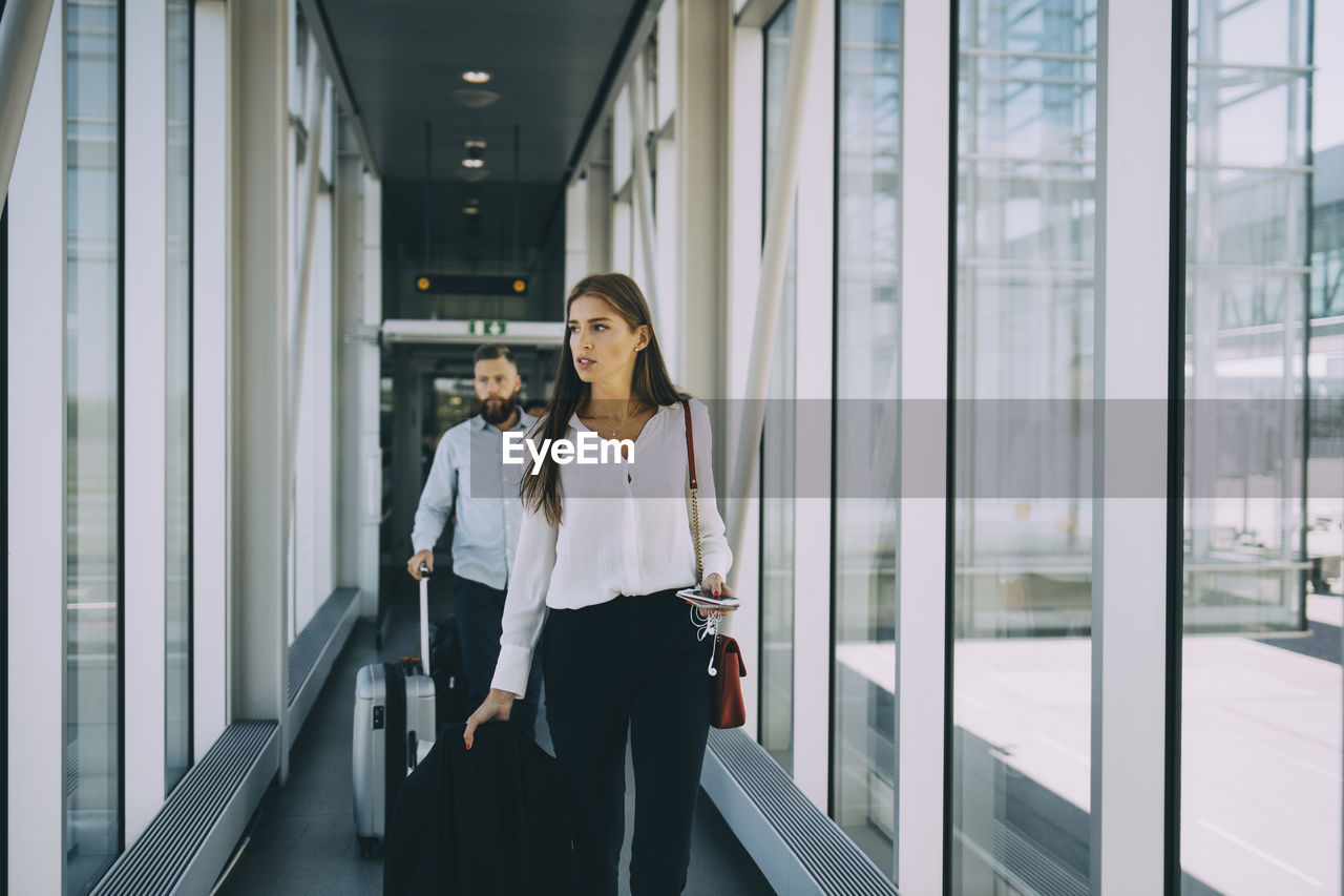 Business colleagues pulling luggage while walking in corridor at airport