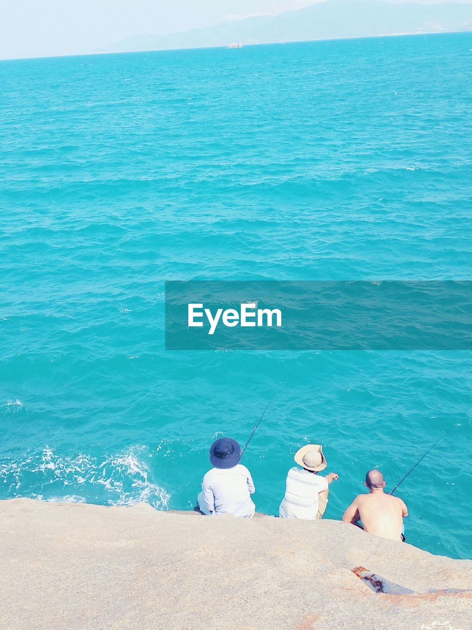 High angle view three men fishing while sitting on rock against sea