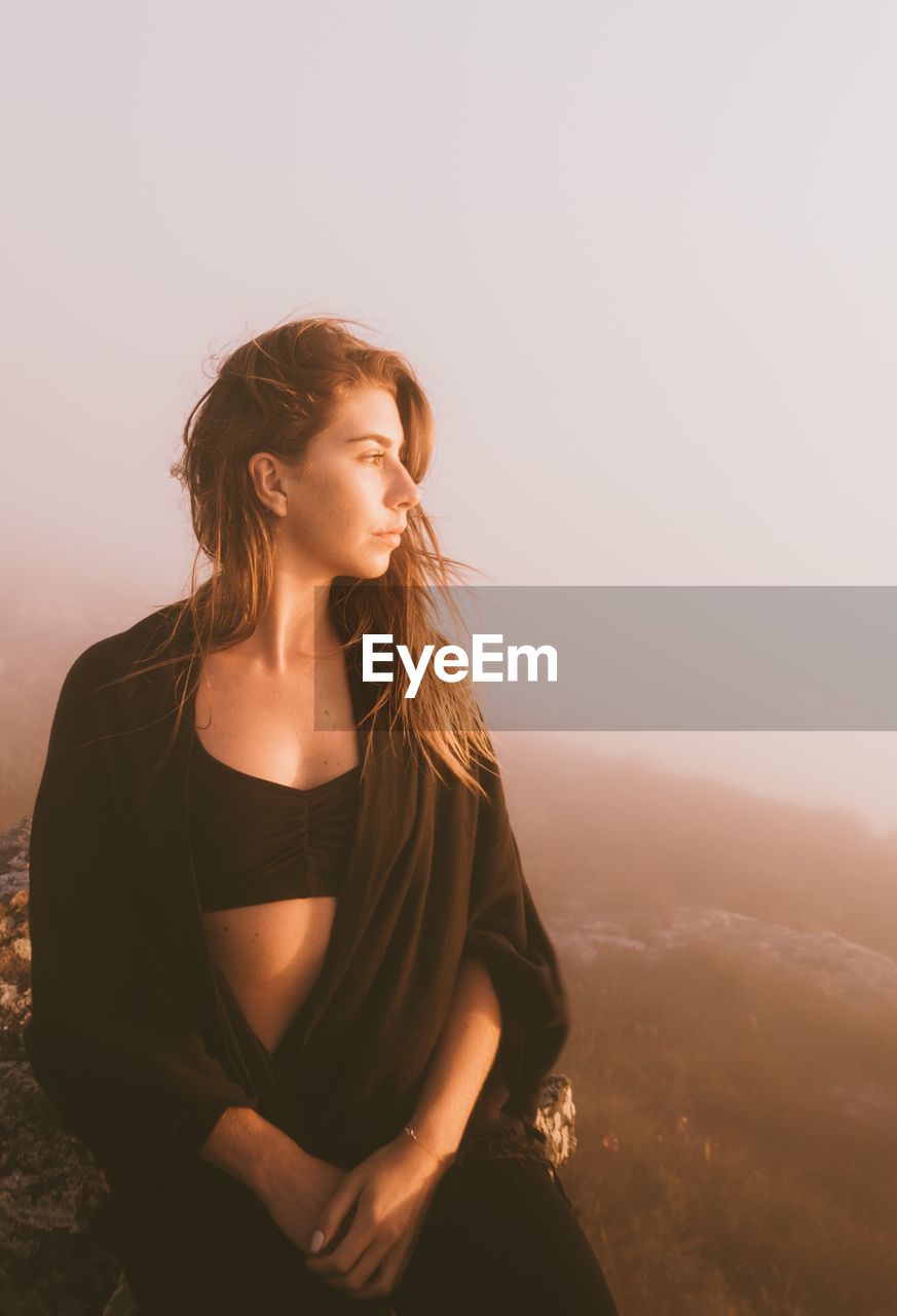 Beautiful young woman looking away standing against clear sky