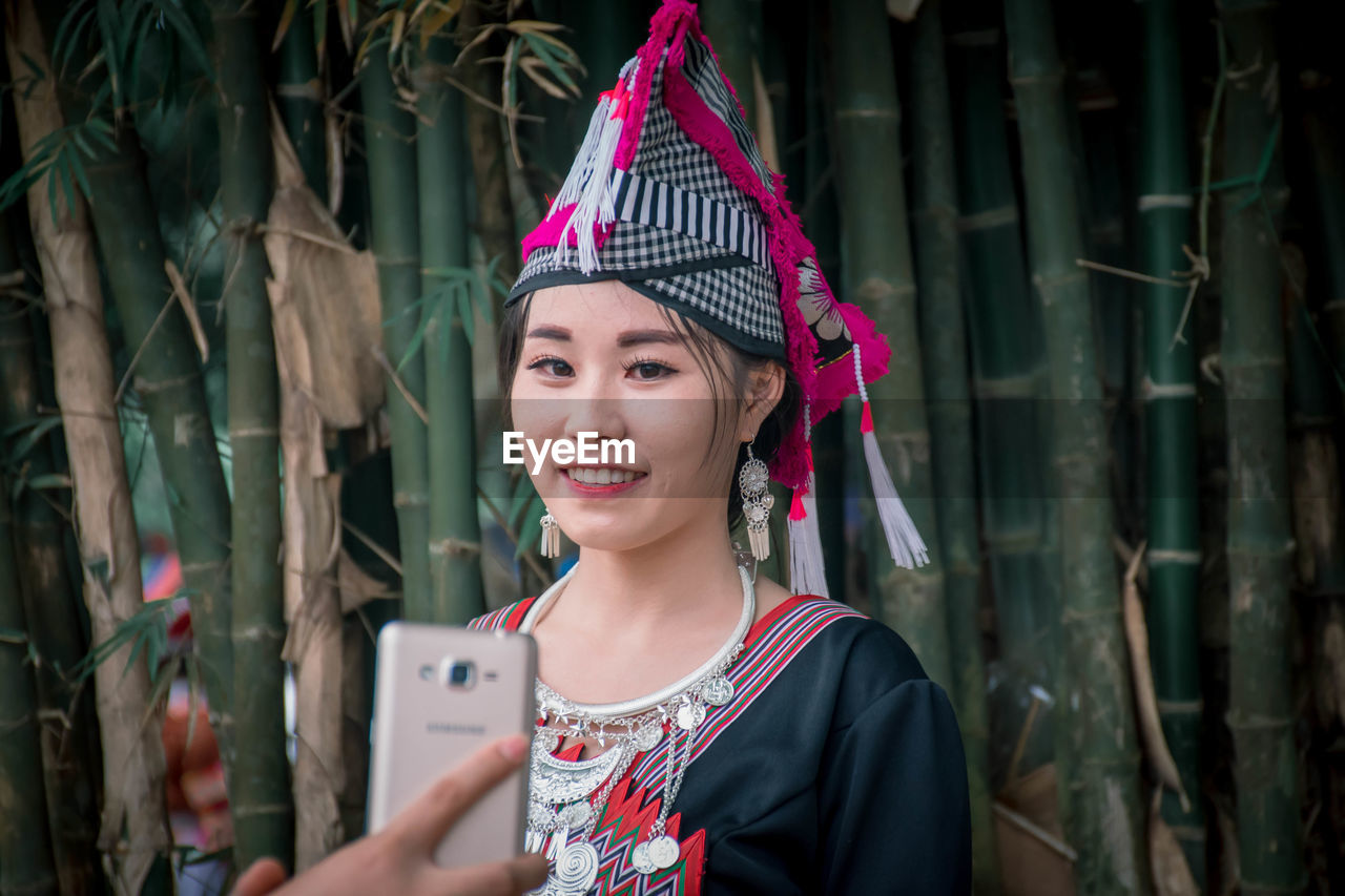 PORTRAIT OF A SMILING YOUNG WOMAN USING PHONE OUTDOORS