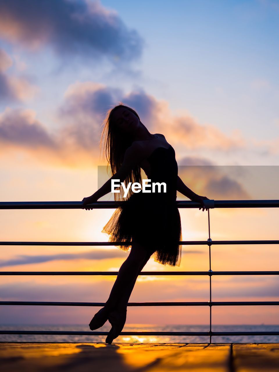 Silhouette woman dancing by railing against sea during sunset