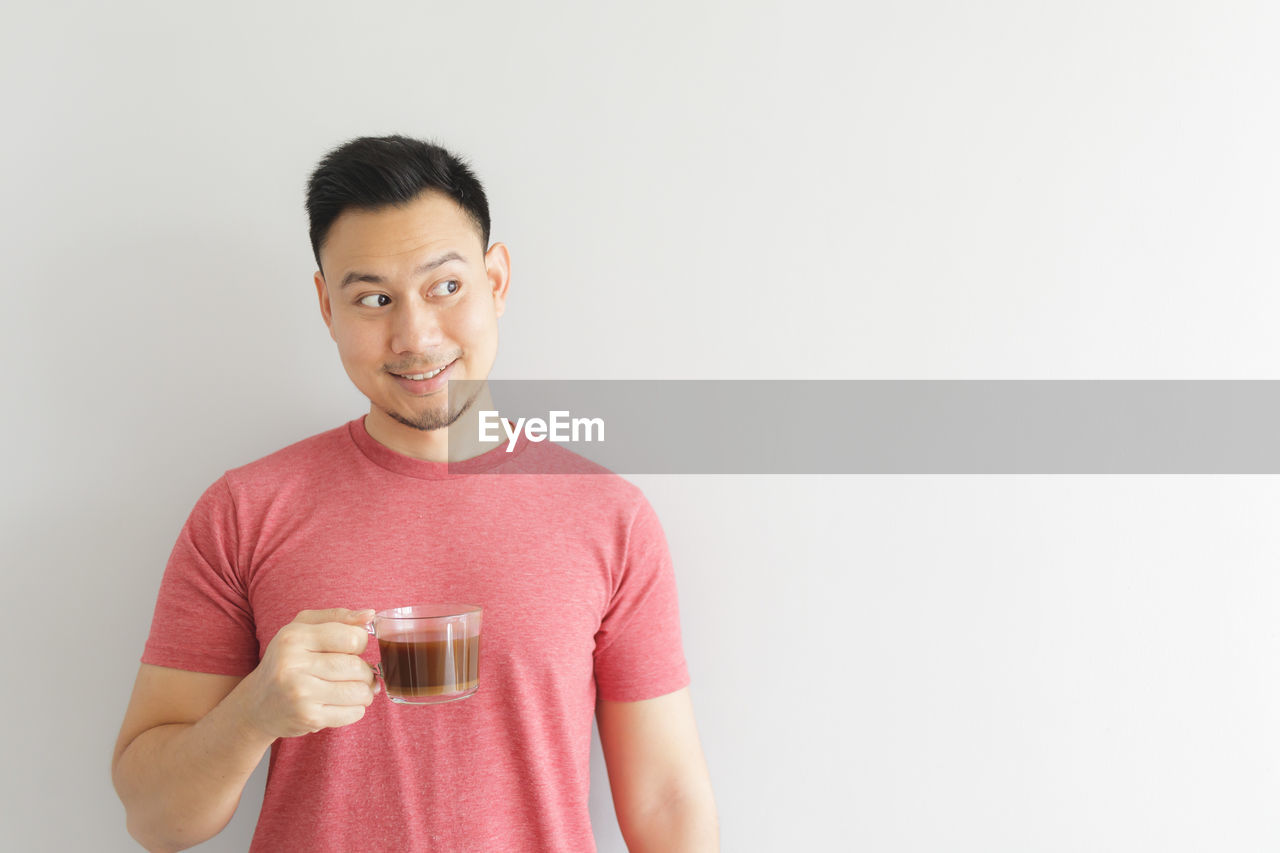 Smiling man looking away while holding tea cup against white background