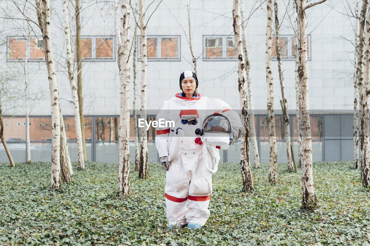 Female astronaut holding space helmet while standing in garden