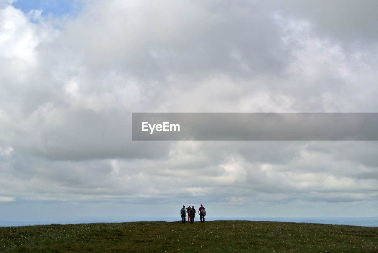 Hikers on hill against cloudy sky