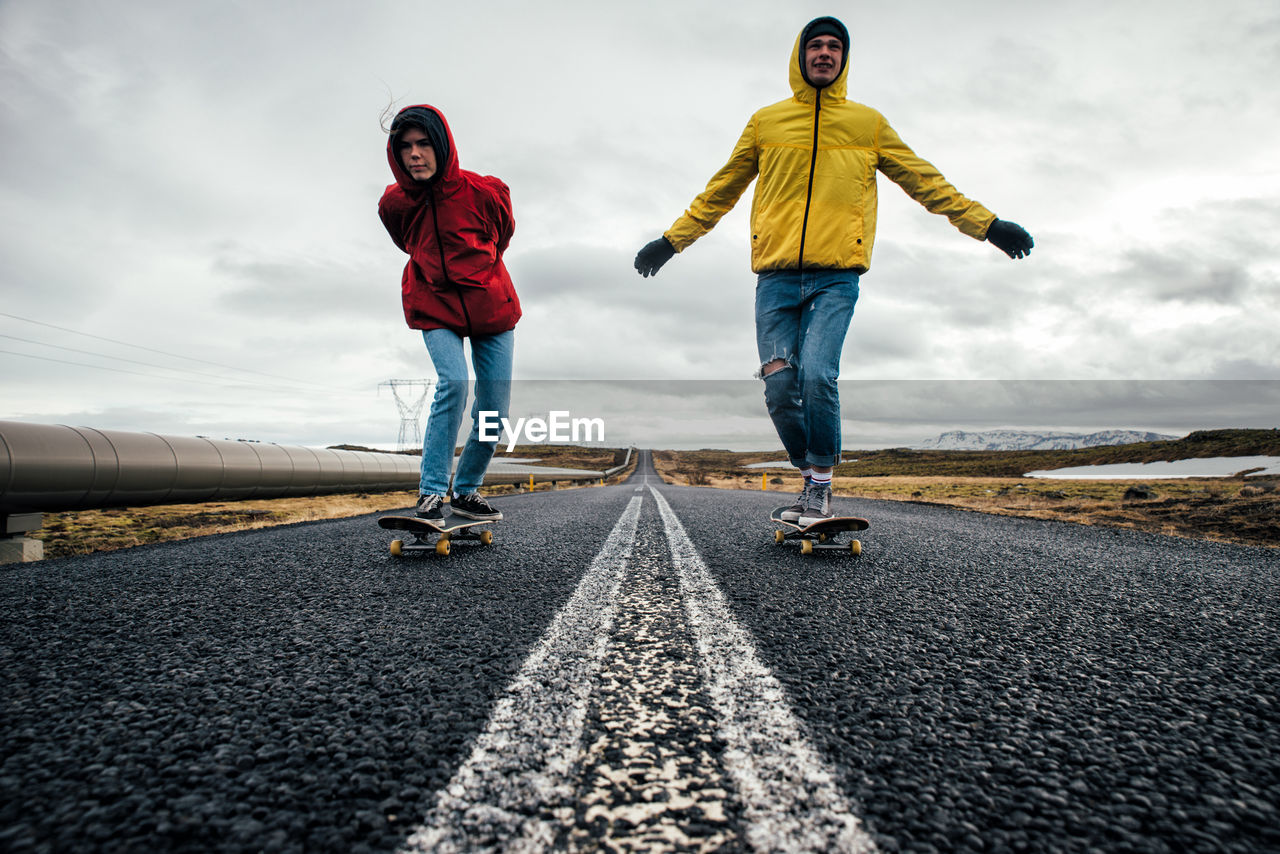 Full length of couple skateboarding on road against sky