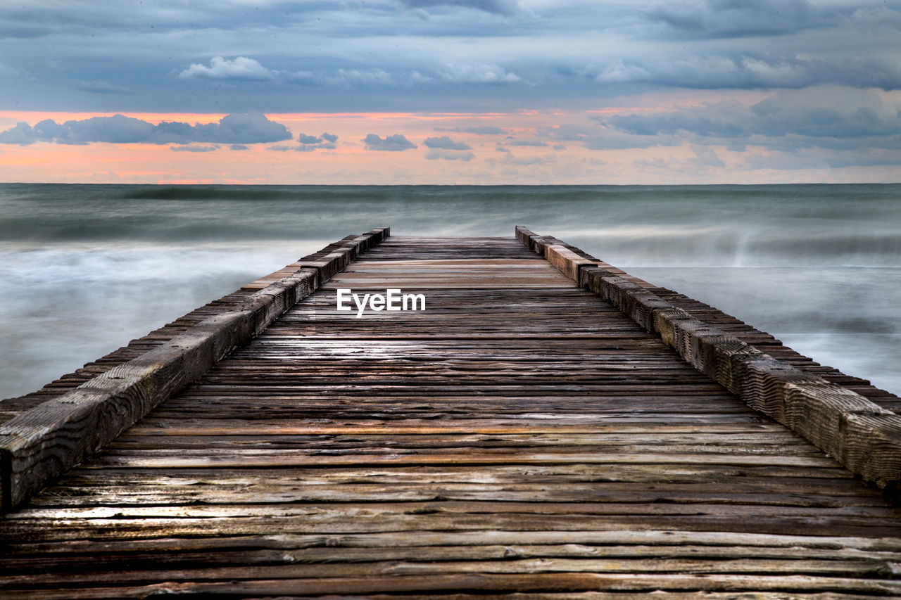 Wooden pier over sea against sky during sunset