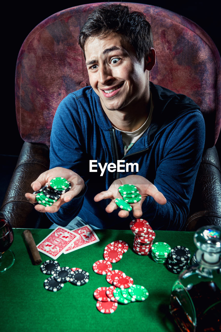 High angle view man sitting with poker chips on table against black background