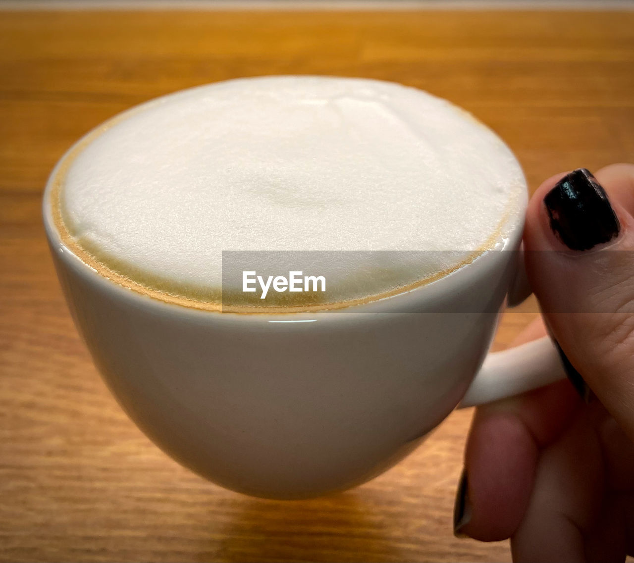 food and drink, drink, hand, refreshment, frothy drink, holding, one person, food, cup, indoors, latte, coffee, mug, close-up, hot drink, table, freshness, coffee cup, cappuccino, lifestyles, focus on foreground, wood, finger, adult