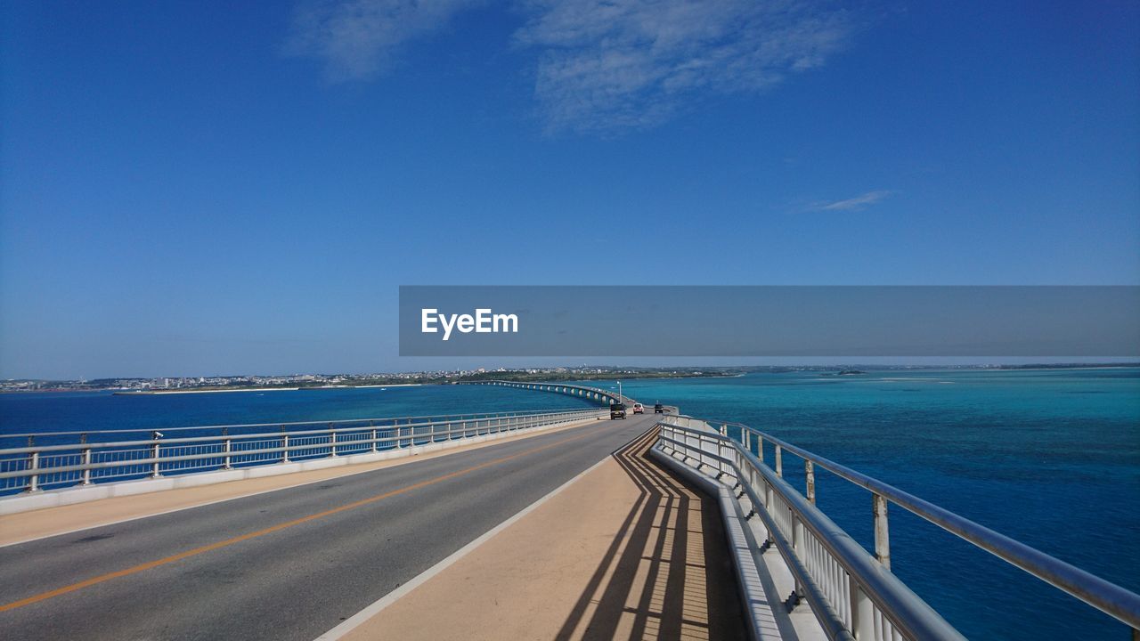 View of road by sea against blue sky