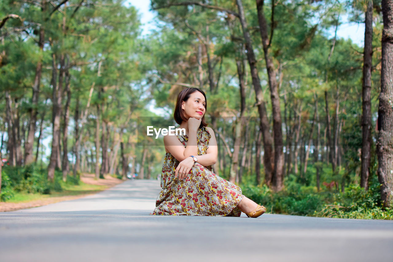 Portrait of woman sitting on road against trees