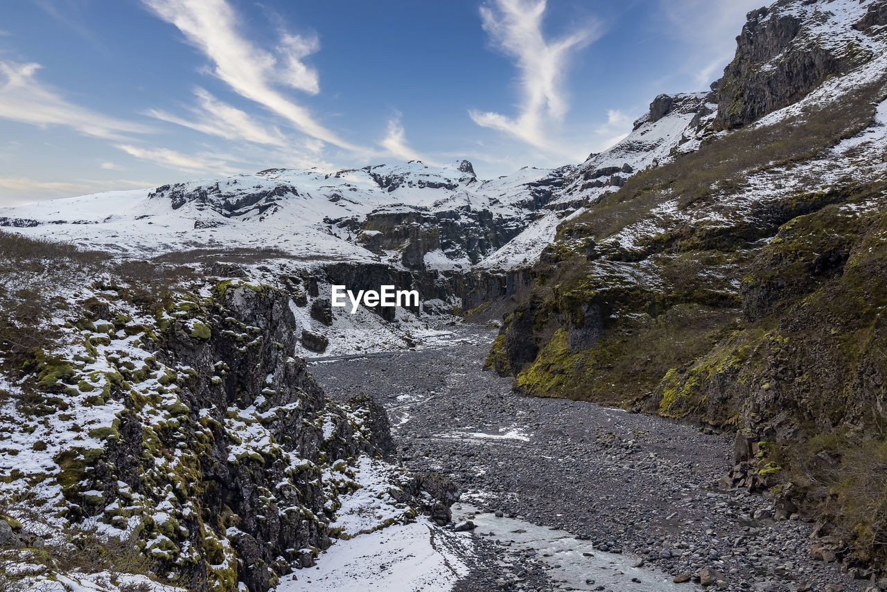 Scenic view of stream amidst snow covered mountains in valley against sky