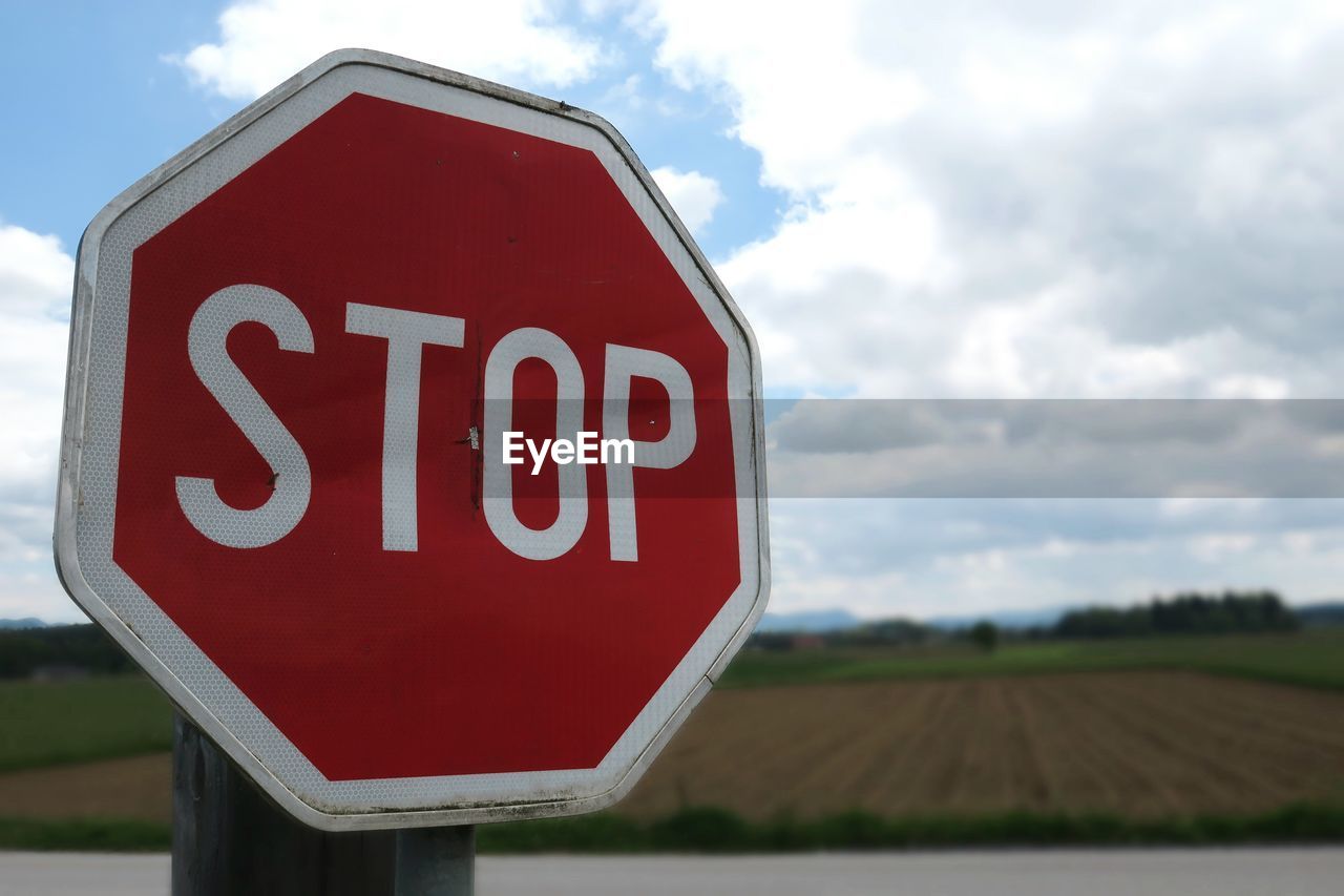 Close-up of stop sign by field against sky