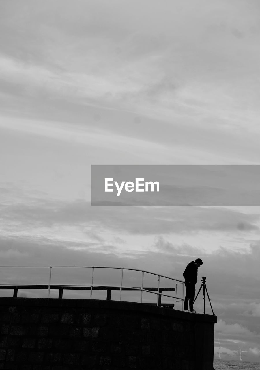 sky, cloud, horizon, silhouette, white, architecture, nature, built structure, one person, sea, standing, men, monochrome, railing, black, black and white, monochrome photography, day, coast, outdoors, full length, water, lifestyles, occupation, ocean, leisure activity, adult, building exterior